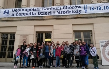 szkolny ch&oacute;r Sereno ze swoją dyrygentką stoi przed Filharmonią Pomorską 