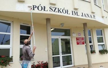 Zdjęcie przedstawia usuwanie napisu Zesp&oacute;ł Szk&oacute;ł im. Jana Pawła II w Łochowie z elewacji szkoły. Sierpień 2017