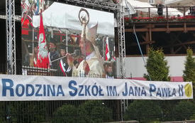 Na zdjęciu widać telebim z wyświetlanym obrazem uroczystości religijnej i napis Rodziny szk&oacute;ł im. Jana Pawła II