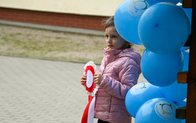 na zdjęciu widać dziewczynkę z biało-czerwonym kotylionem w dłoni i niebieskie balony