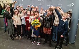 na zdjęciu widać grupę dzieci z nauczycielem wskazujących chłopca z ż&oacute;łtymi tulipanami