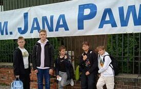 na zdjęciu widać uczni&oacute;w na tle baneru z napisem "Imienia Jana Pawła II"