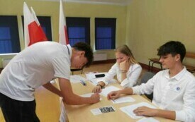 na zdjęciu widać podpisującego listę wyborcza ucznia i uczni&oacute;w z komisji wyborczej