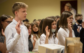 Na zdjęciu widać uczni&oacute;w z podniesiona prawą ręką składających przysięgę absolwenta