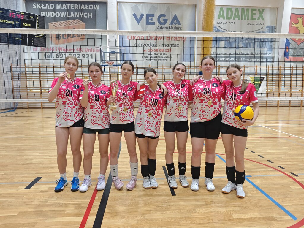 Zawodniczki drużyny siatkarskiej z&nbsp;SP Łochowo pozują do zdjęcia w&nbsp;strojach sportowych z&nbsp;medalami na&nbsp;sali gimnastycznej.