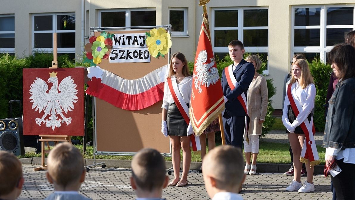 Tęskniliśmy za wami Na zdjęciu widać uczniów z pocztu sztandarowego w strojach apelowych oraz grupę uczniów z klas pierwszych i nauczycieli