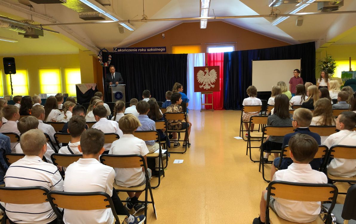 Zakończenie 2022 Na zdjęciu widać uczniów siedzących na krzesłach i słuchających przemówienia pana dyrektora.