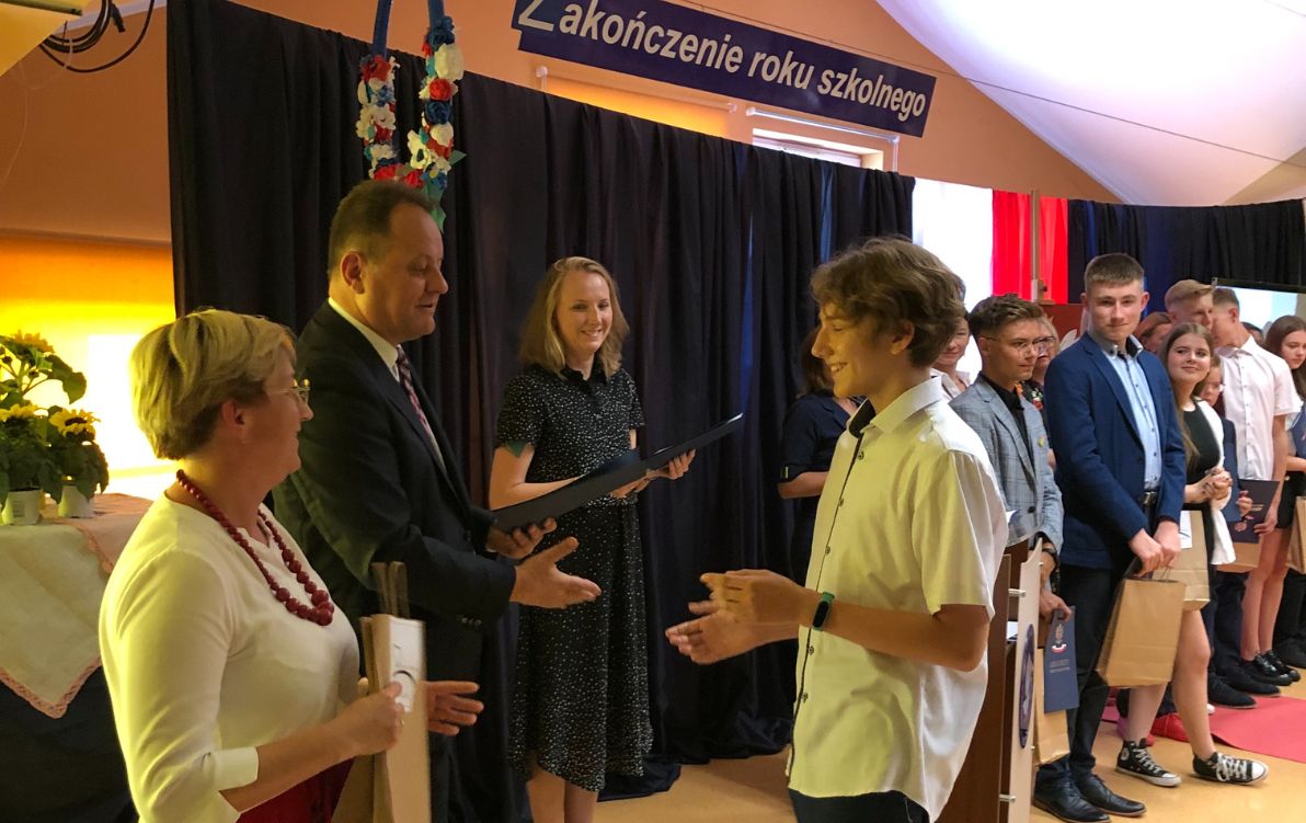 Zakończenie klas 8 Na zdjęciu widać ucznia odbierającego świadectwo z rąk pana dyrektora. W tle znajdują się uczniowie w rzędzie, którzy odebrali już swoje świadectwo