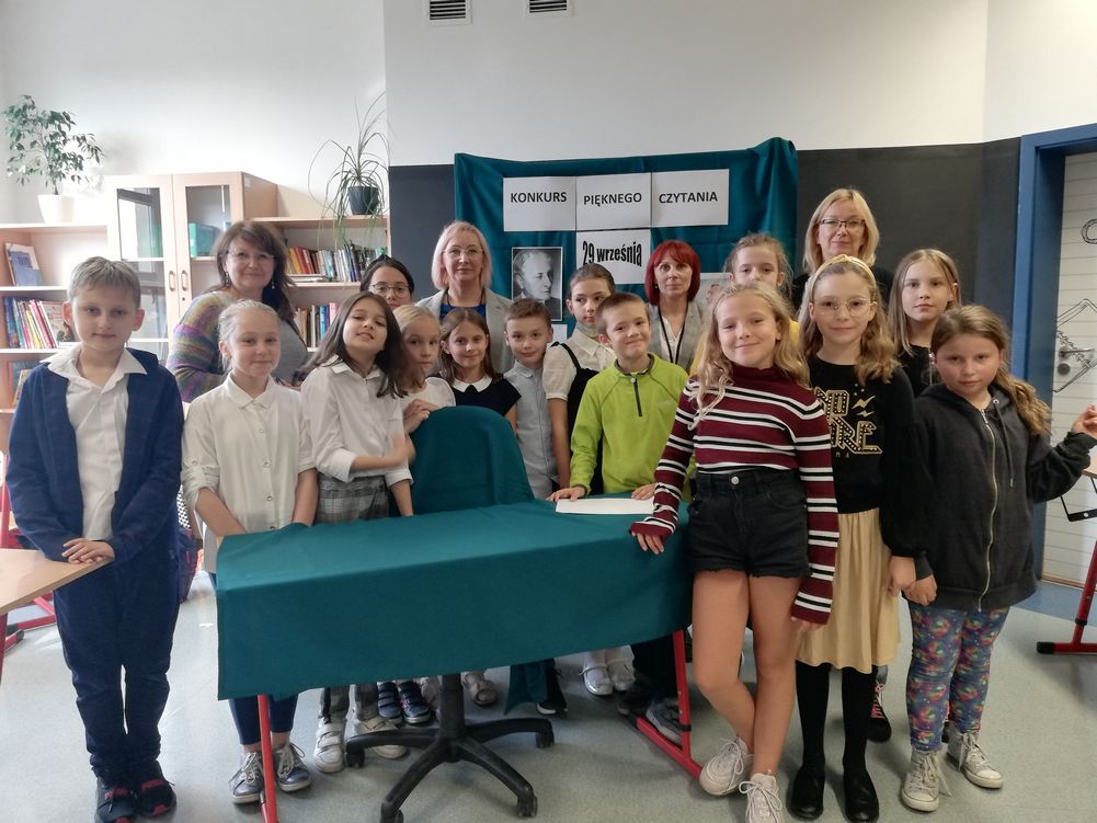 Konkurs głośnego czytania Na obrazku widać grupę uczniów z nauczycieli na tle regałów z książkami