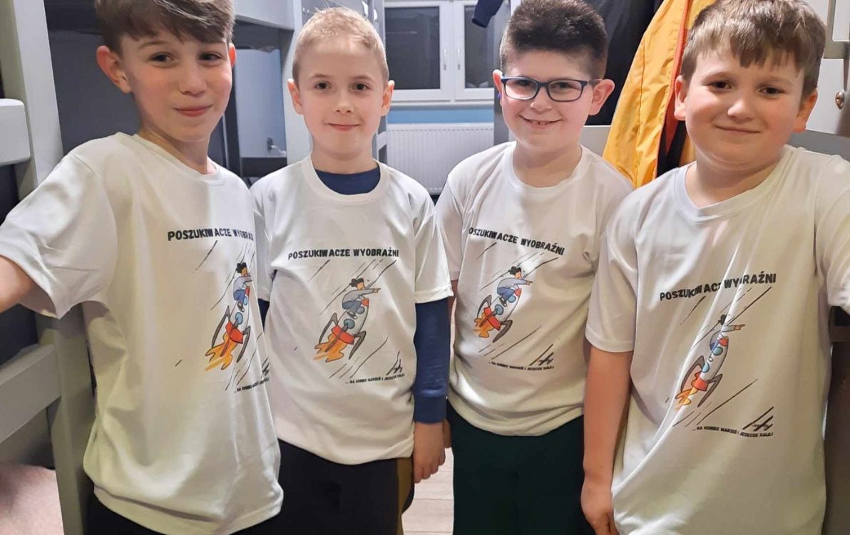 Czterech chłopc&oacute;w wieku 7-8 lat pozuje do zdjęcia w&nbsp;identycznych białych t-shirtach z&nbsp;logiem Odysei