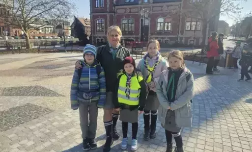 Zdjęcie przedstawia drużynową pozującą z czterema uczestnikami biegu zuchów na tle budynku z czerwonej cegły.