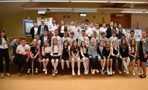 Na zdjęciu uczniowie klas 3a i 3d siedzący na scenie w strojach galowych, po przedstawieniu z okazji Narodowego Święta Konstytucji 3 Maja.