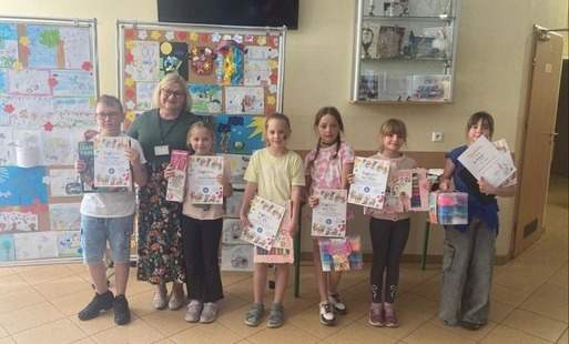 Zdjęcie przedstawia laureatów konkursów plastycznych organizowanych przez świetlicę szkolną pozujących z wicedyrektor Anną Podgórską na placu Karolka, w tyle wystawa prac uczniów.