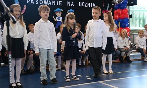 Zdjęcie przedstawia uczniów klas 1 na środku sali gimnastycznej, którzy zostali wytypowani do prowadzenia ceremonii pasowania na pierwszoklasistę.